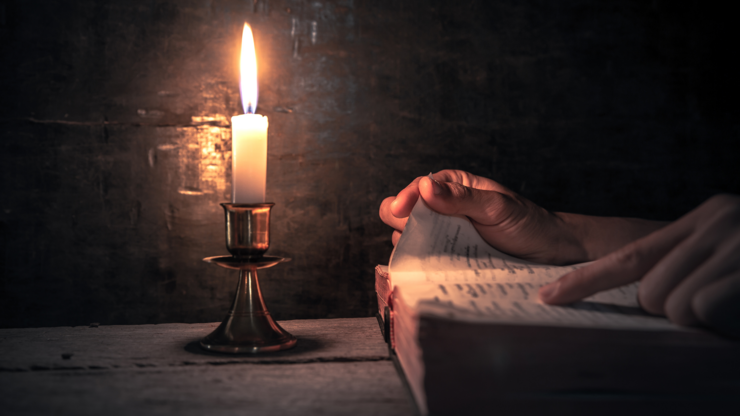Close up hands holding and reading the Bible with light of candle on wooden table at worship room. christian concept.