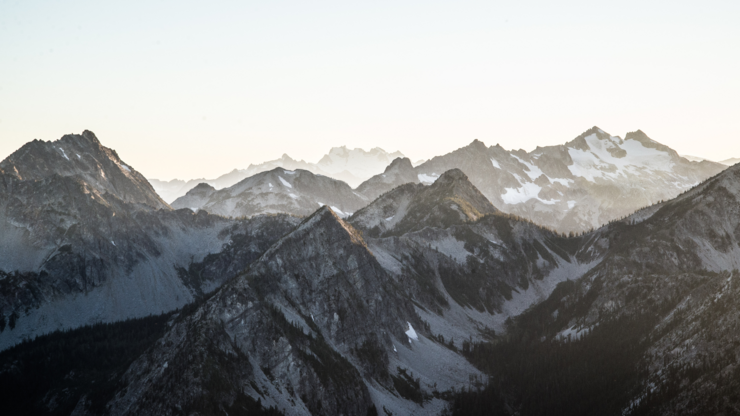Majestic mountains bathed in soft morning light, highlighting their peaks and valleys against a clear sky.