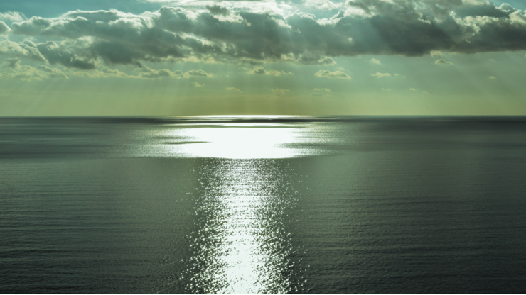 A large body of water reflecting sunlight as it shines through scattered clouds above.