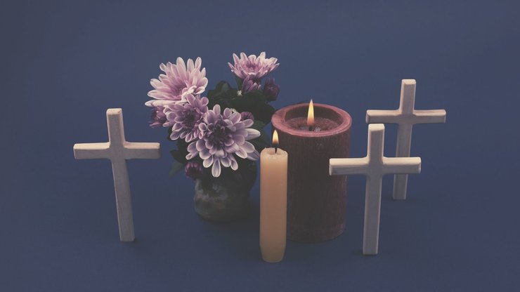 Composition of burning candle, flowers and wooden cross for all souls day. Also suitable for funeral, mourning, grief. High angle view.