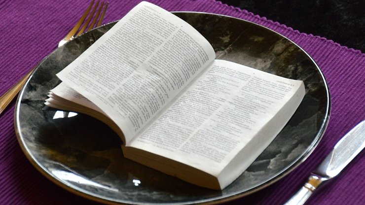 bible opened up at Matthew 4:4 on a plate with silverware and a purple placemat